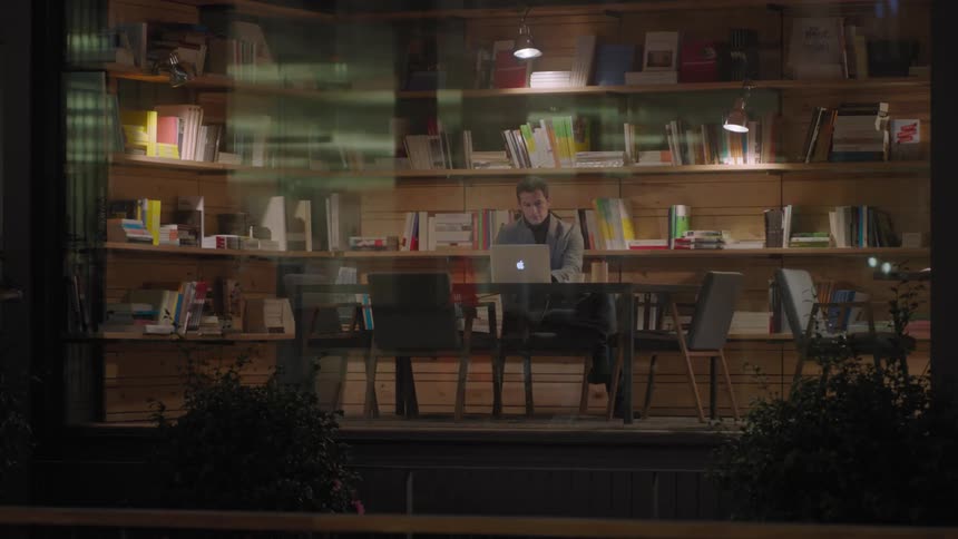 A man sits at a library desk using a laptop