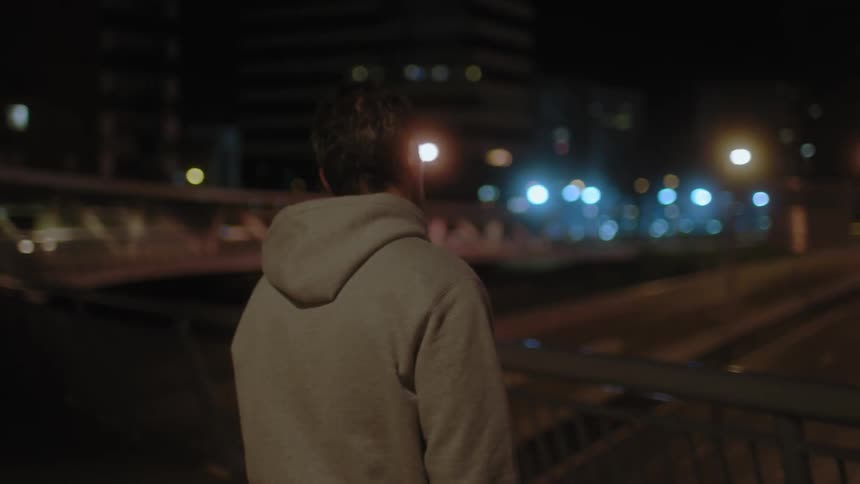 A man in sweats is taking a break on a bridge overlooking a busy highway