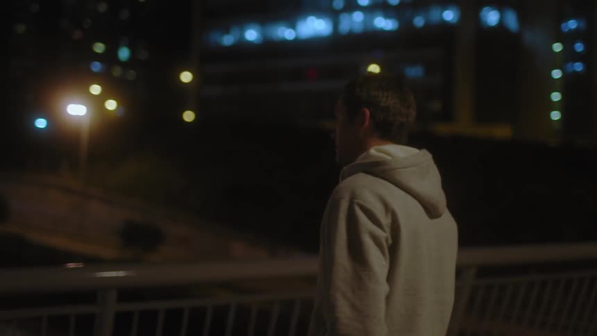 A man in sweats is looking over the edge of a bridge onto the expressway below