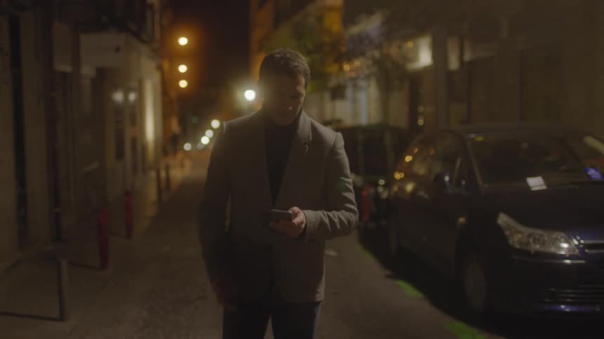 A man is walking down a small street looking at her phone