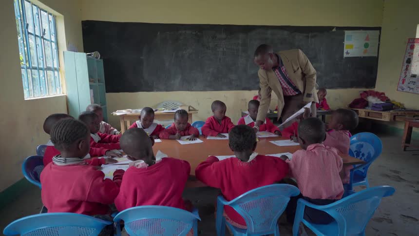 Teacher passes out markers to children seated at a large table