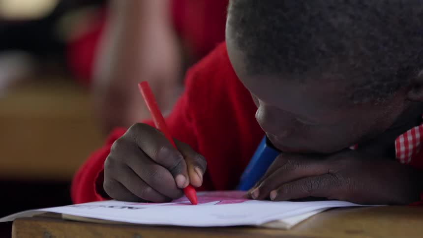 A boy colors with a red crayon at school
