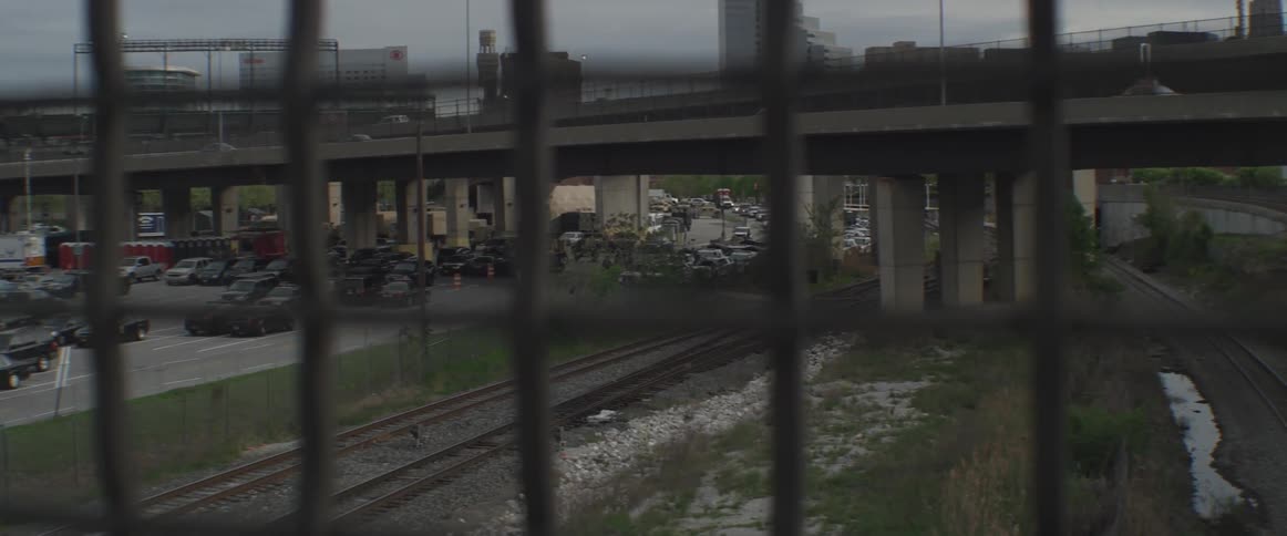 Vehicles fill a parking lot next to train tracks below a bridge