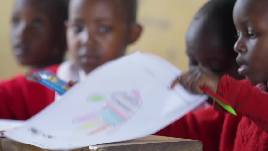 School kids sit at desks with crayons and paper
