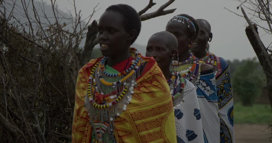 Group of maasai wearing costumes walk single file outside