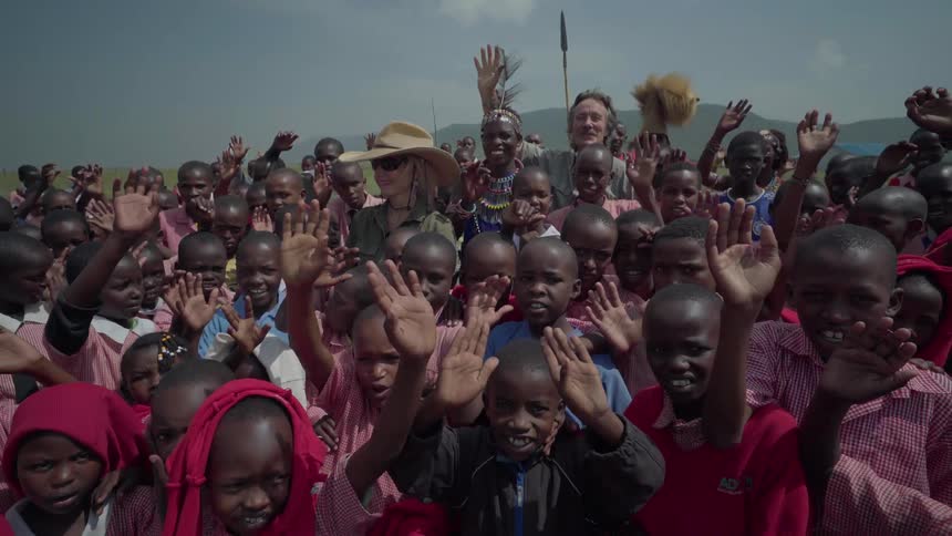 A crowd of children stand around two adults