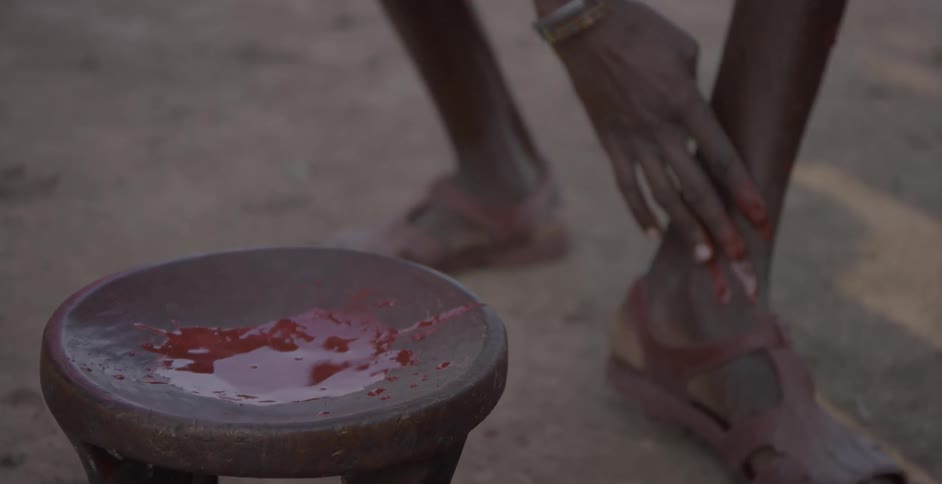 Maasai putting red paint on his legs