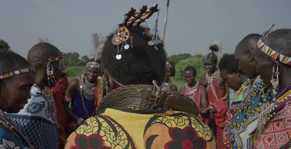 Maasai in native dress stand outside smiling and talking