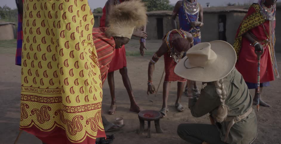 Group of maasai stand outside and touch liquid on a small metal stand