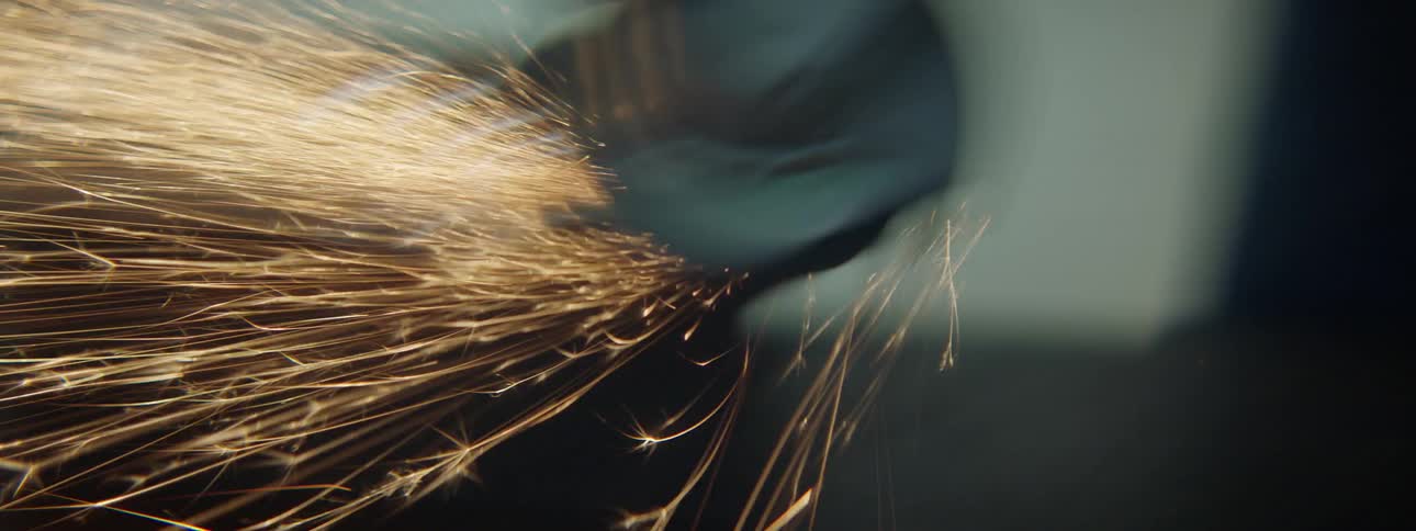 Sparks fly from a power tool a man is using in a workshop