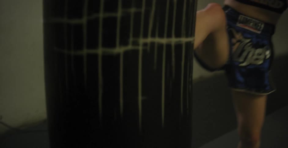 Woman kicks a punching bag while wearing boxing gloves