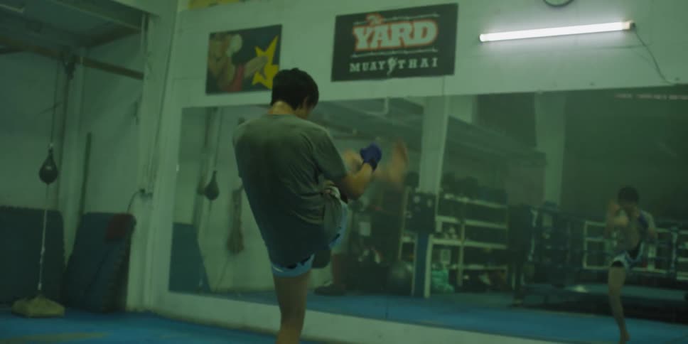 Athlete kicking a leg high repeatedly while practicing in a gym in front of a large mirror