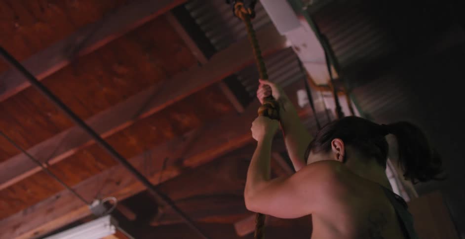 A woman climbs up a rope in a gym
