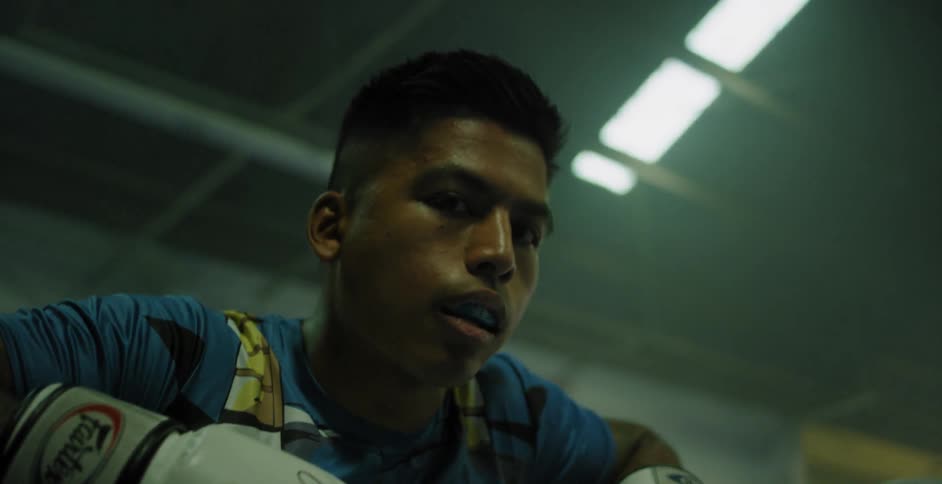 A boxer is leaning on the ropes wearing white gloves