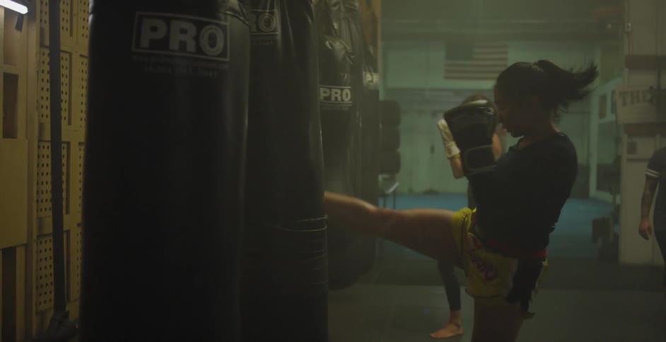 Two women kick heavy bags in a gym