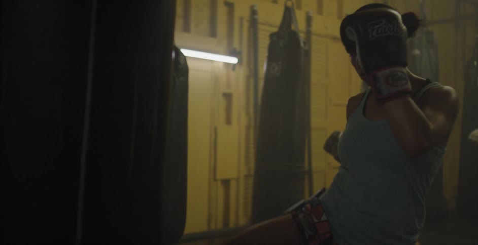 Woman wearing boxing gloves kicks at a heavy bag