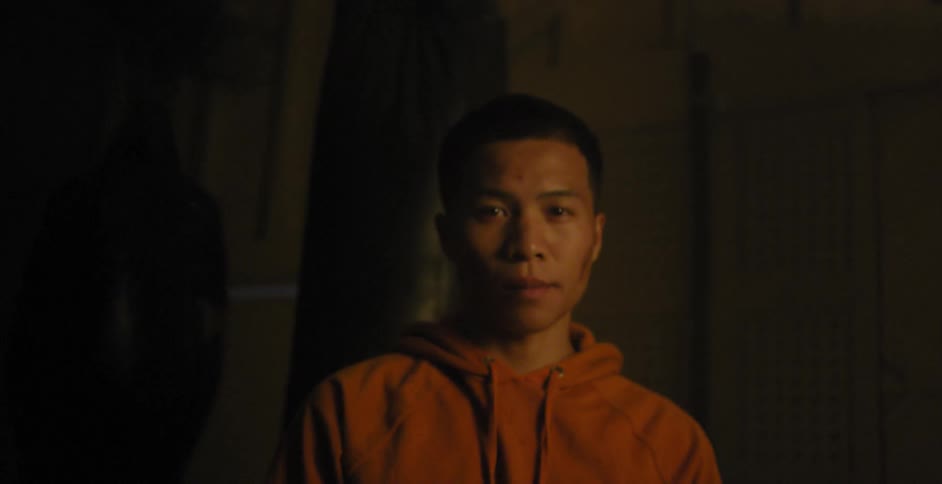 A man stands in front of a heavy bag in a gym