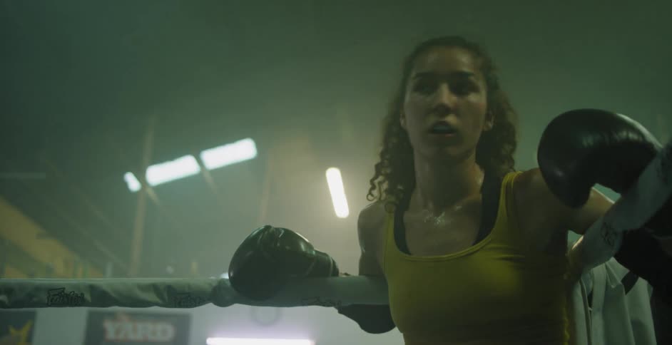 A female fighter is resting in the corner of a boxing ring