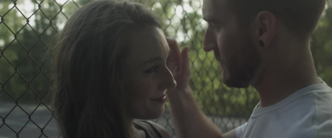 A man and woman are hugging and kissing by a fence