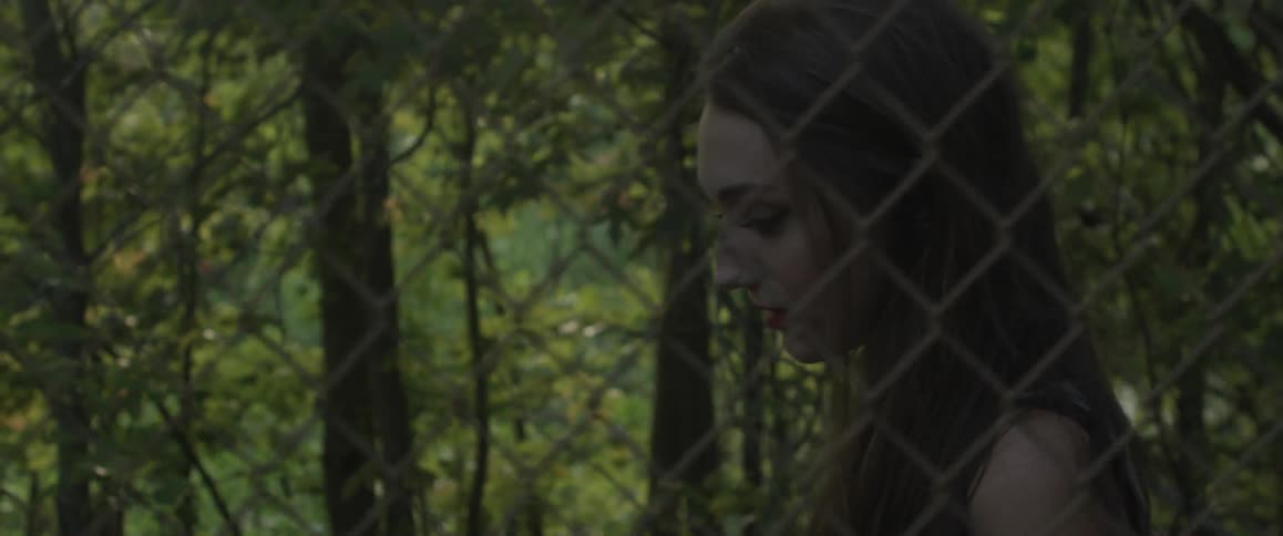 A woman walks along a chain link fence and trees