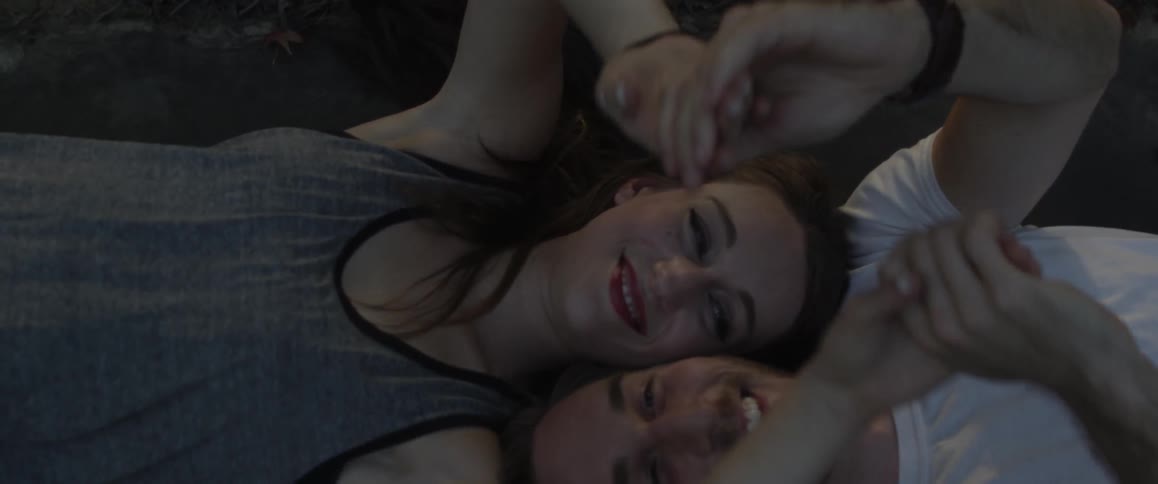 A couple lay on the ground holding hands and waving around