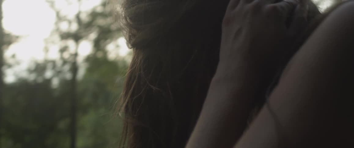 A woman scratches her head in the woods