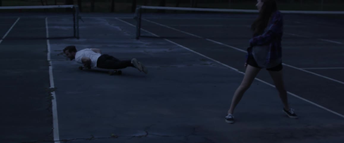 A man is laying down on a skateboard and rides between a woman's legs