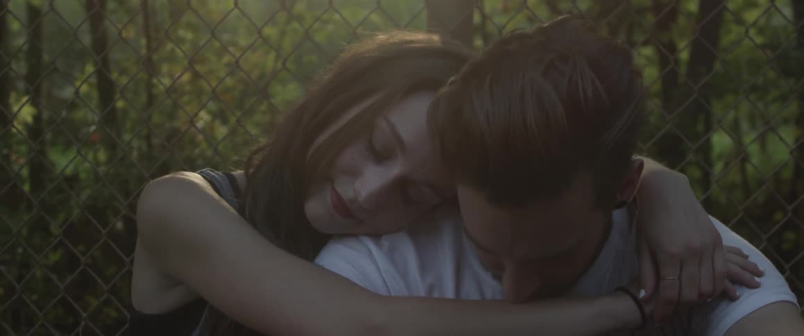 Man and woman cuddle next to a chain link fence