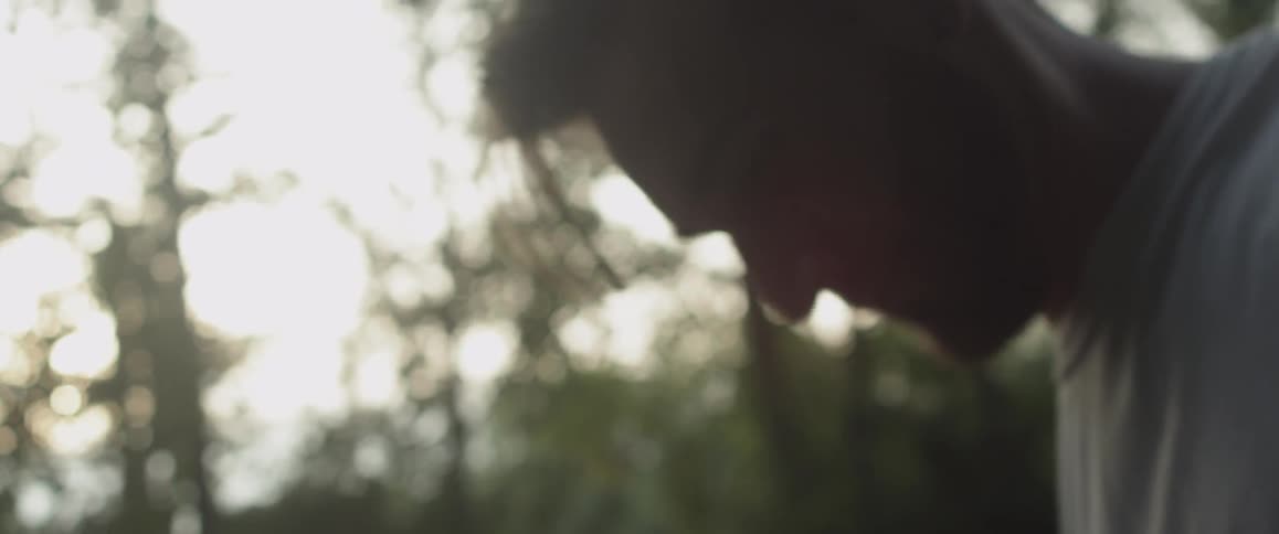 A man rubs his head and walks away in the forest
