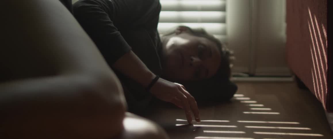 A woman lies on the floor playing with shadows cast from a window