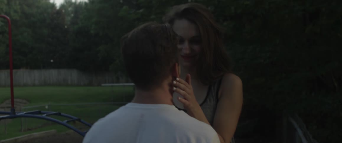 A woman is caressing a man's face as they stand outside at a playground