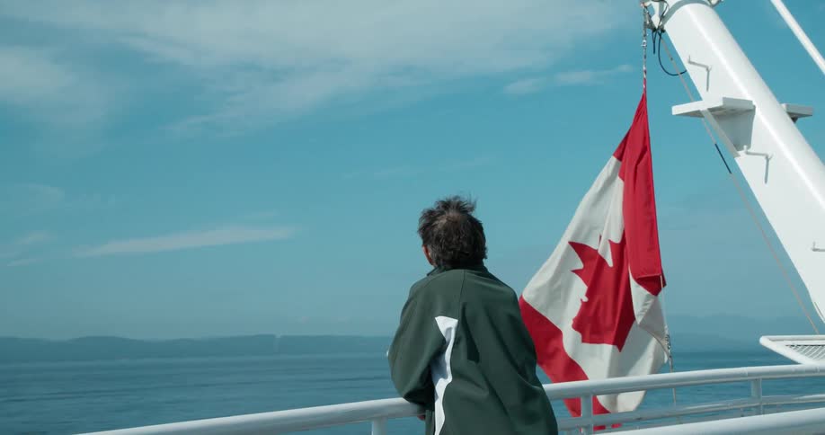 Man overlooks the side of a moving ship with a canadian flag