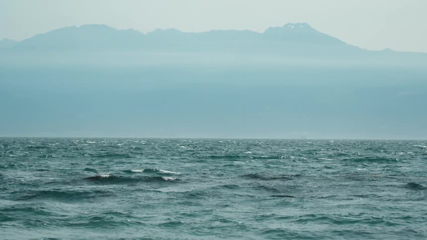 Ocean waves rise and fall off a mountainous coastline during the day