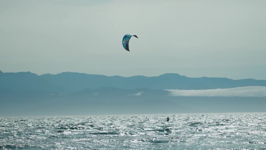 A kiteboarder travels across the waves on a hazy day
