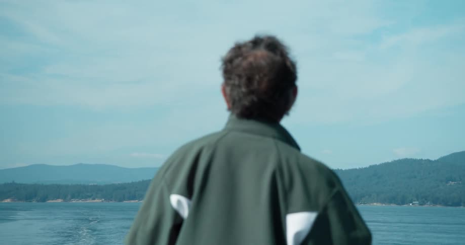 A man on a boat watches the shoreline receding in the distance
