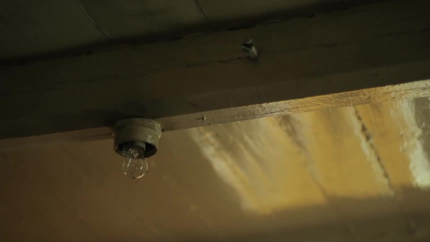 A bare light bulb attached to a wooden ceiling beam