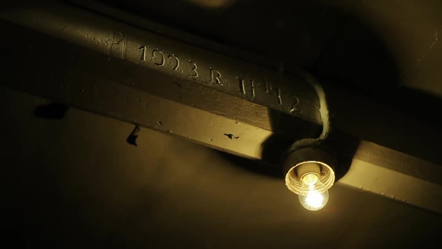A single light bulb suspended from a beam with numbers on it stays lit