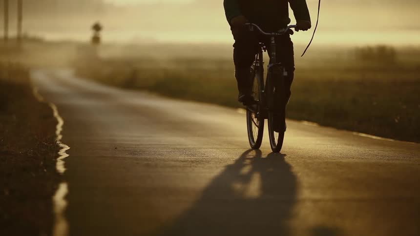 A person bikes down a road at sunset