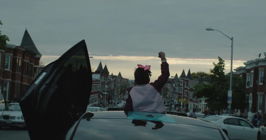 A person stands through a sunroof with their fist in the air