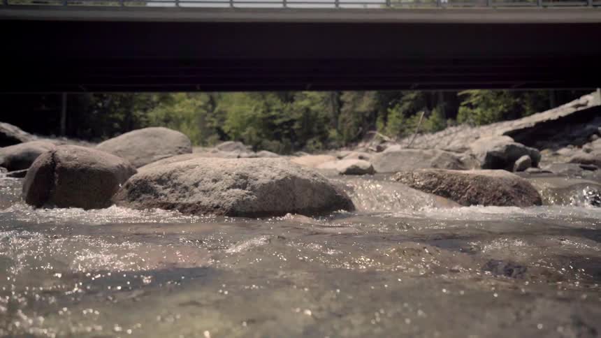 Water flows over rocks in a river near a bridge