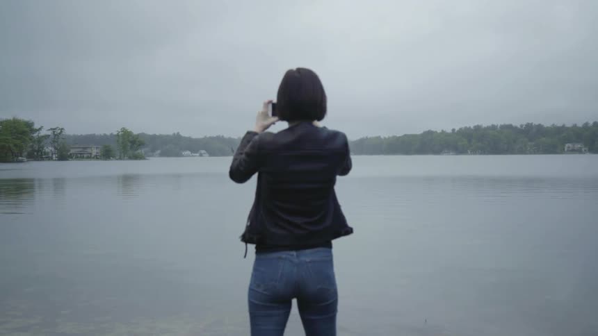 A woman takes a photograph near a lake