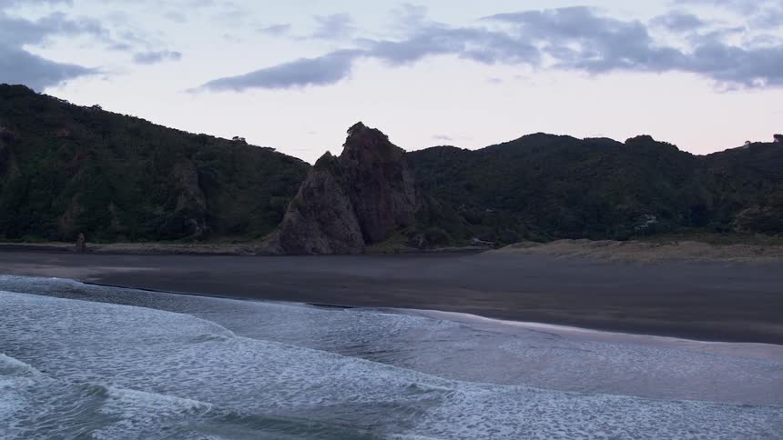 Waves roll onto the shore of a beach at the base of a cliff