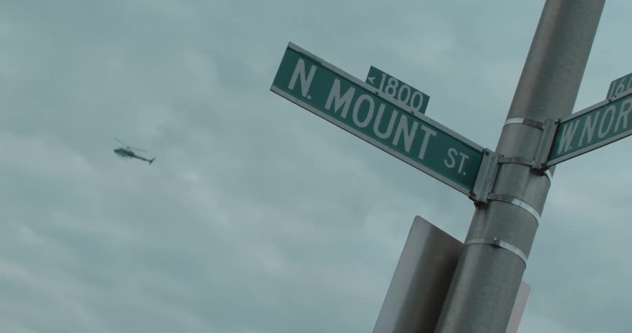 Street signs mounted on a pole with a helicopter high up in the sky