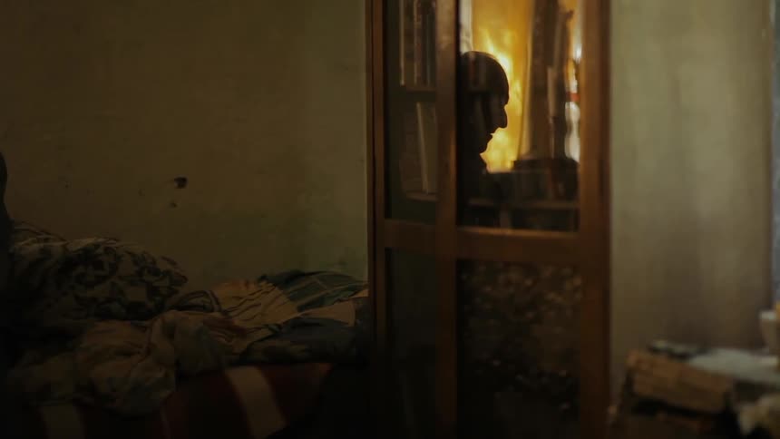 The reflection of an old man is seen in a door window of a disorderly room