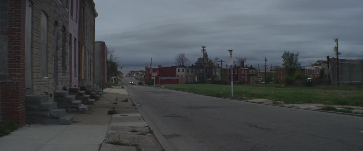 A quiet street with a vacant lot and tenement houses