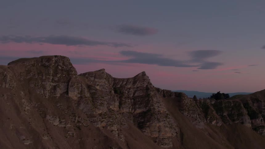 Dusk is falling beyond a canyon in a desert landscape