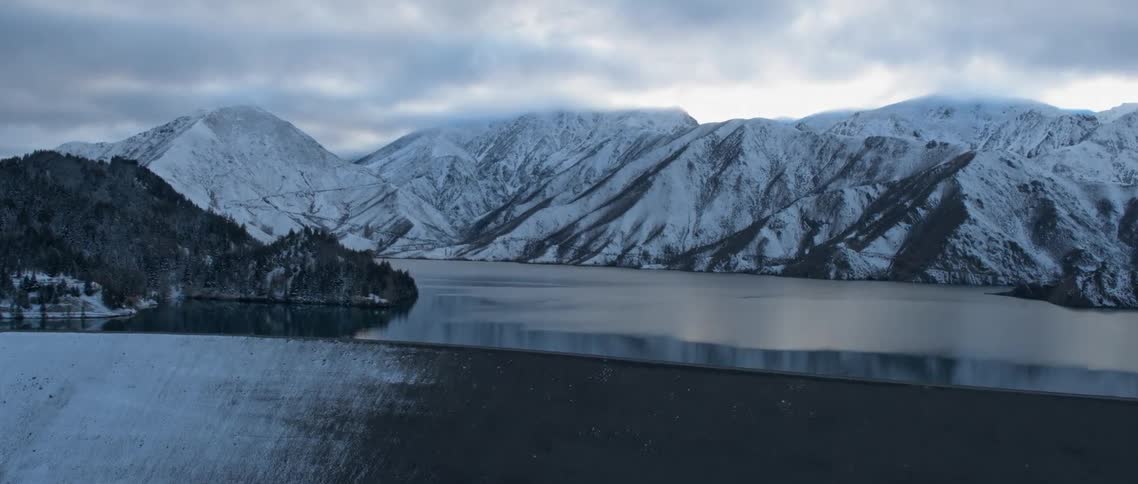 Clouds hover above snow-covered mountains and a reservoir
