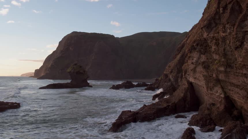 Waves crash over rocks and at the base of cliffs
