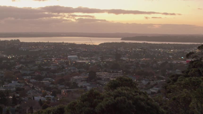 The sun sets behind a forest over a large city