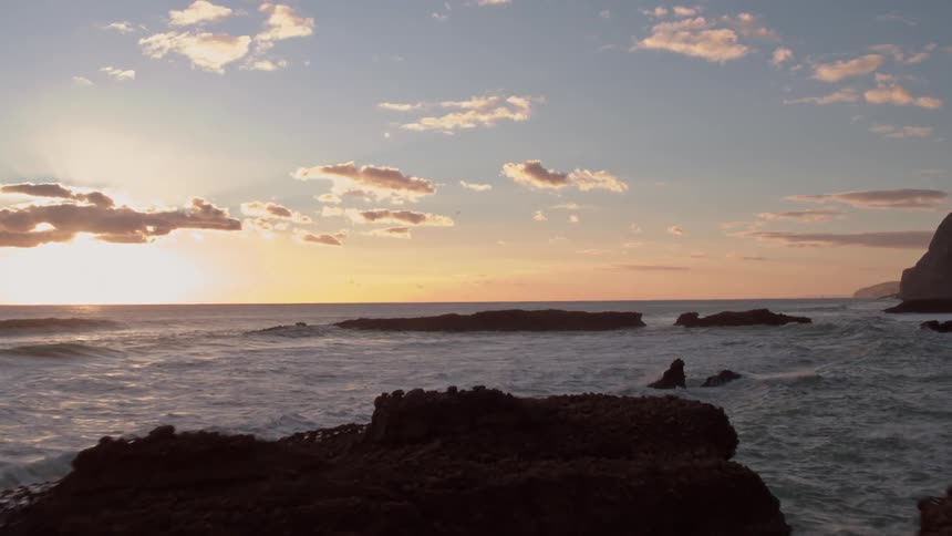 Ocean waves splash over rocks along the coast at sunset